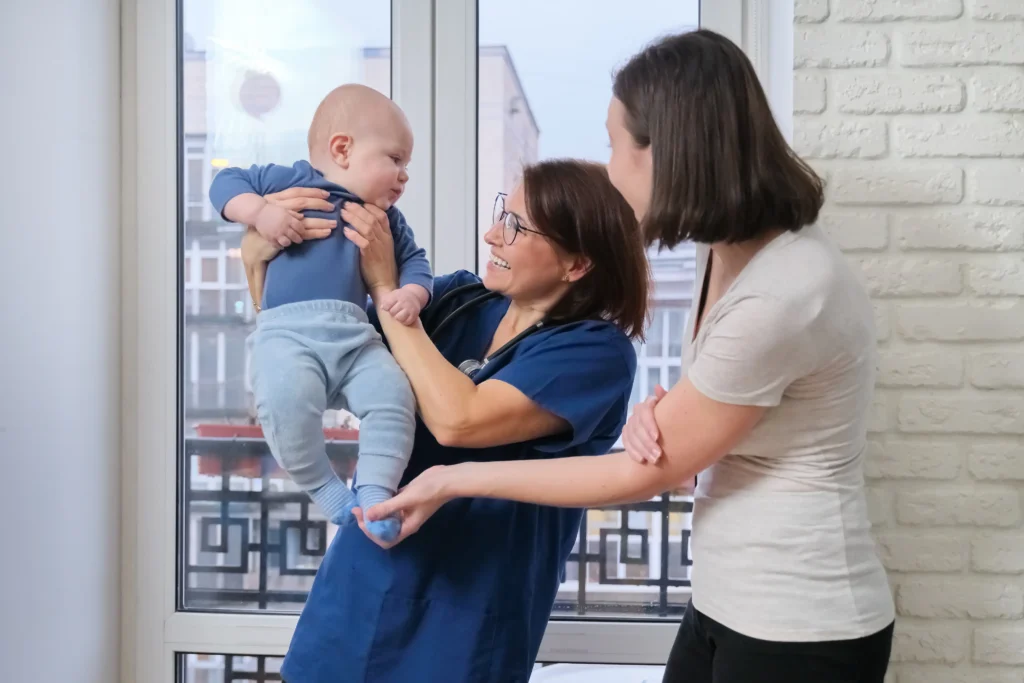 Female doctor examining toddler child. Pediatrician took baby in arms, talking with her mother and laughing together. Pediatrics, care and health of children up to one year