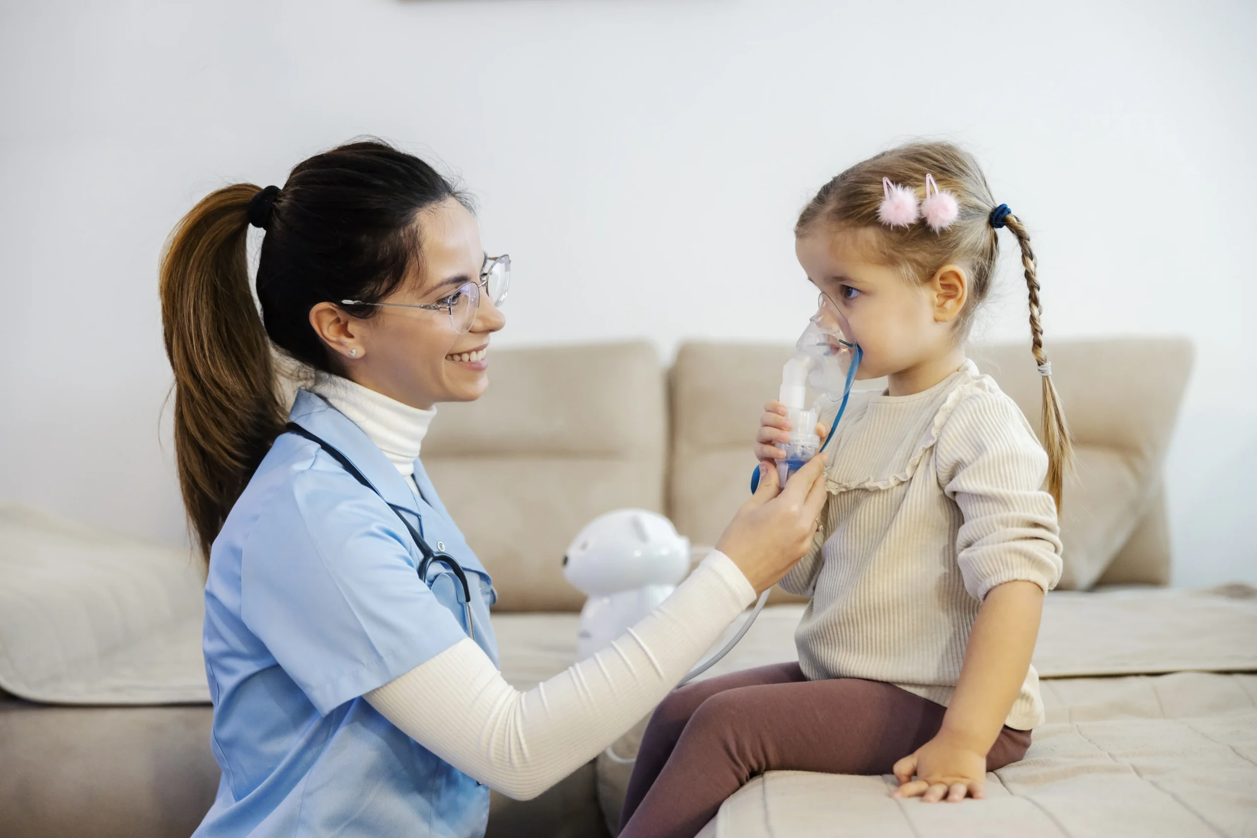 A little girl is inhaling medicine through nebulizer and her pediatrician in helping her during her home visit.