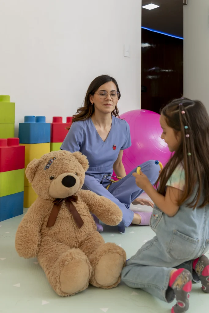Young female pediatrician interacting with a little girl and a teddy bear, creating a comfortable and playful atmosphere in the doctor's office