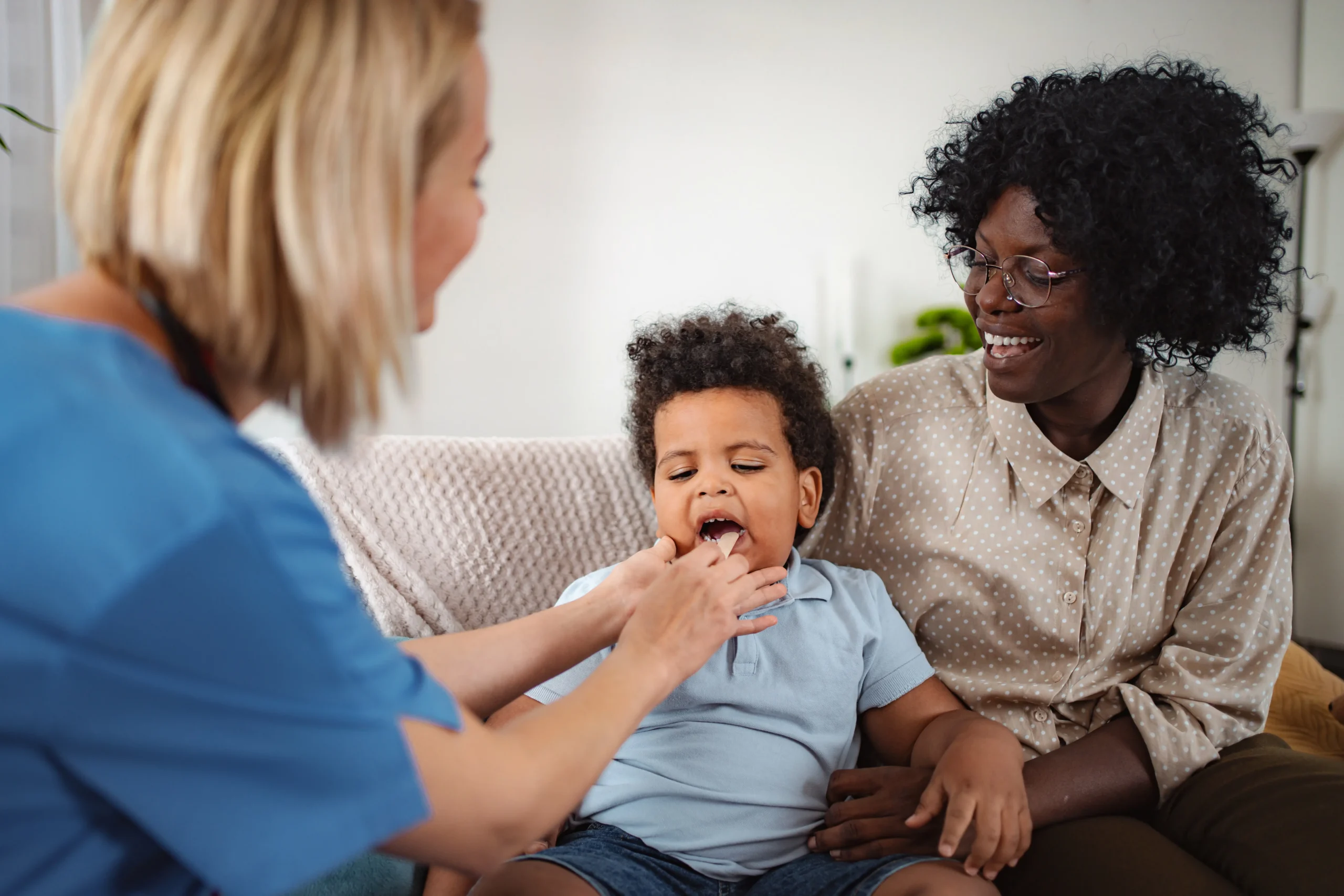 Pediatric nurse examining a child's throat while mother watches with a smile